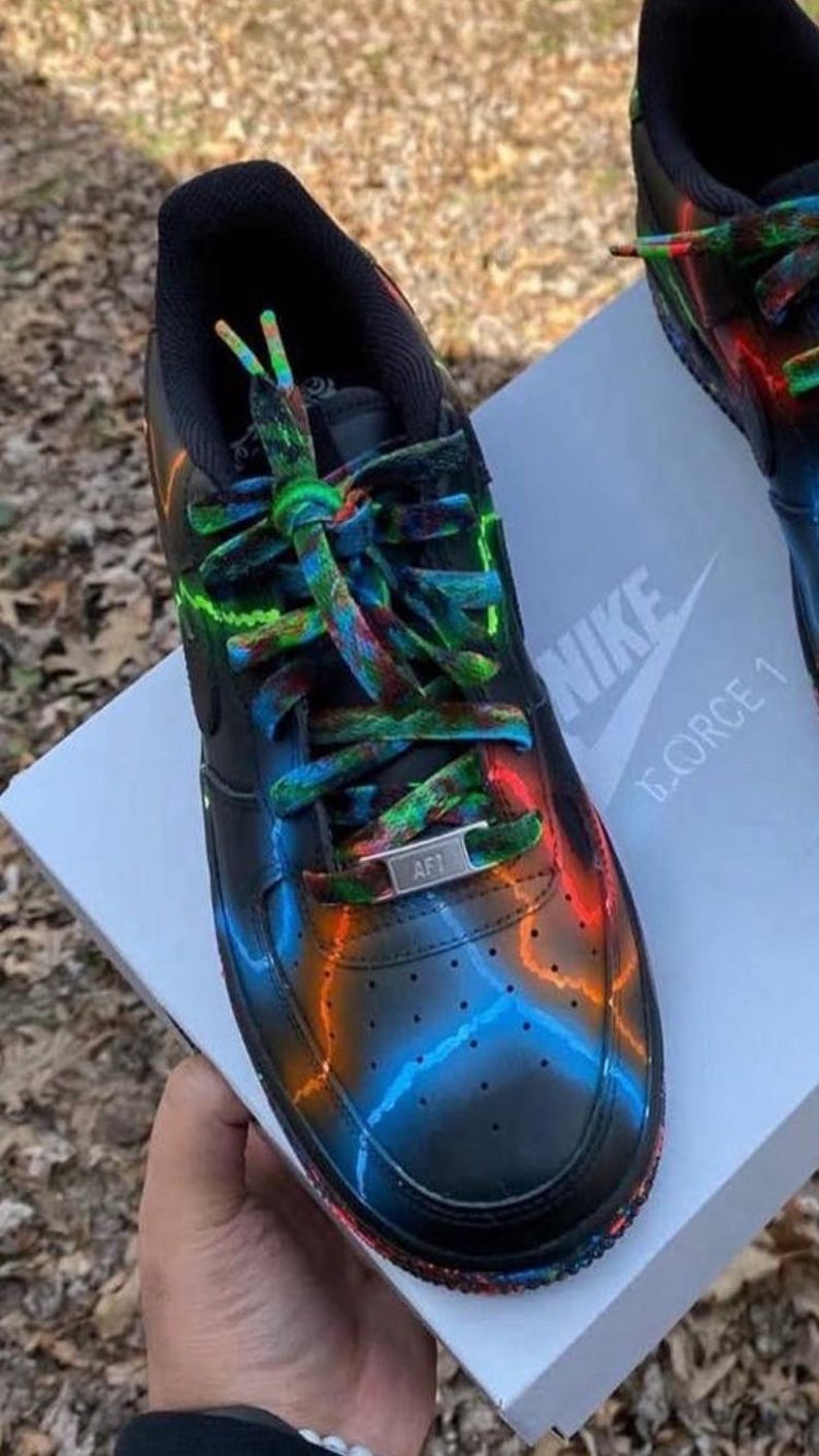 Pu&ograve; includere: Scarpe da ginnastica Nike Air Force 1 nere con accenti neon colorati. Le scarpe presentano una base nera con vivaci disegni blu, arancioni e verdi. I lacci sono multicolori e la linguetta mostra il logo Nike. Su una scatola bianca.