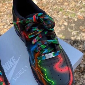 Pu&ograve; includere: Sneakers Nike Air Force 1 nere con accenti neon colorati e lacci coordinati. Le scarpe presentano un design vivace con striature rosse, verdi e blu. Il logo Nike e "FORCE 1" sono visibili sulla scarpa e sulla scatola.
