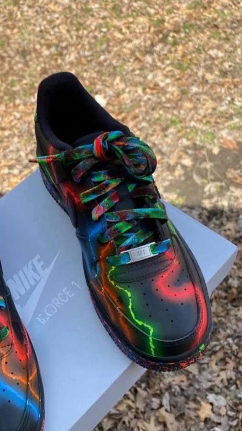 Pu&ograve; includere: Sneakers Nike Air Force 1 nere con accenti neon colorati e lacci coordinati. Le scarpe presentano un design vivace con striature rosse, verdi e blu. Il logo Nike e "FORCE 1" sono visibili sulla scarpa e sulla scatola.