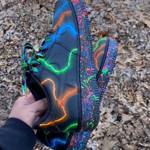 Pu&ograve; includere: Scarpe da ginnastica nere con fulmini neon verdi, arancioni e blu. Le suole sono ricoperte di schizzi di vernice colorati e i lacci sono arcobaleno. Un design di calzature unico e artistico.