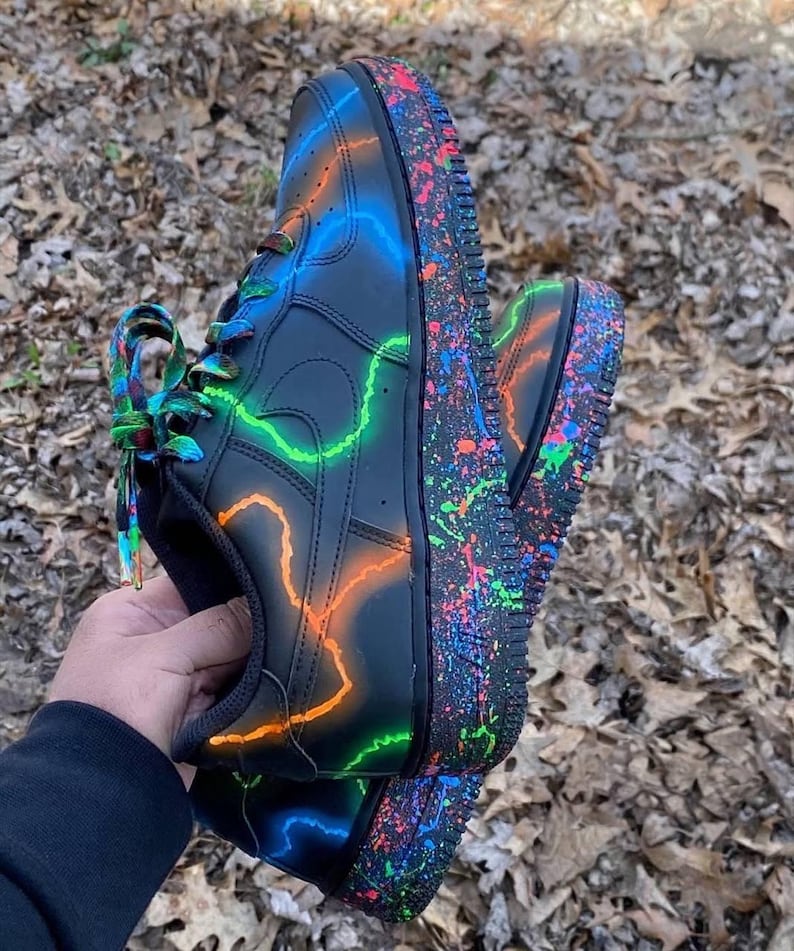 Pu&ograve; includere: Scarpe da ginnastica nere con fulmini neon verdi, arancioni e blu. Le suole sono ricoperte di schizzi di vernice colorati e i lacci sono arcobaleno. Un design di calzature unico e artistico.