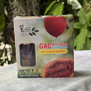 K&ouml;nnte beinhalten: Eine quadratische Pappschachtel f&uuml;r das Bio Way GAC Anti-Aging Gesichtsserum. Die Verpackung zeigt eine rote, stachelige Gac-Frucht, einen Querschnitt der Frucht und ein Sichtfenster mit einer dunkelbraunen Flasche. Der Text umfasst GAC Anti-Aging Facial Serum, GMP ISO und Herbal Natural Product.