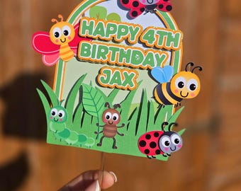 May include: A colorful birthday cake topper featuring cartoon insects and the text "HAPPY 4TH BIRTHDAY JAX." The design includes a ladybug, bee, butterfly, caterpillar, and ant, set against a green and white background.