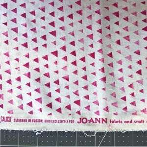 May include: White fabric with a repeating pattern of magenta triangles. The fabric is labeled "Keepsake Calico" and "JOANN fabric and craft stores". The fabric is suitable for sewing and crafting projects.