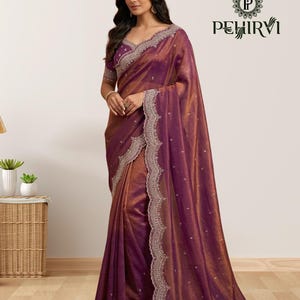 May include: A deep purple and copper-toned saree featuring a shimmering fabric texture, intricate silver embroidery along the scalloped borders, and small silver floral motifs scattered across the drape, with the Pehirvi logo in the corner.