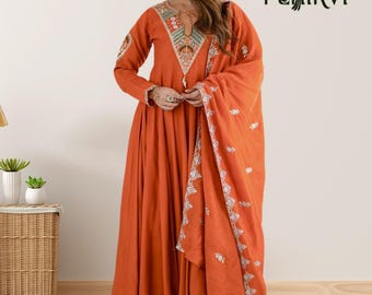 May include: An orange long-sleeved A-line dress featuring a V-shaped neckline with intricate multi-colored embroidery, matching orange trousers, and a coordinating orange shawl with white floral embroidery along the border and the Pehirvi logo.