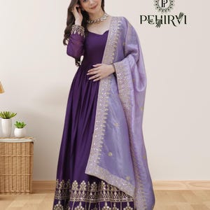 Peut inclure: Une longue robe violette avec des broderies dorées complexes sur l'ourlet. La robe a des manches longues et une écharpe lavande assortie avec des ornements dorés. L'ensemble est élégant et adapté aux occasions spéciales.