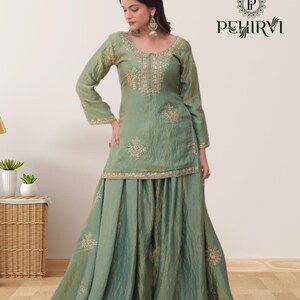 May include: A sage green, long-sleeved outfit with gold embroidery. The top has a scoop neckline and the skirt is floor-length. The outfit is from the brand PEHIRVI.