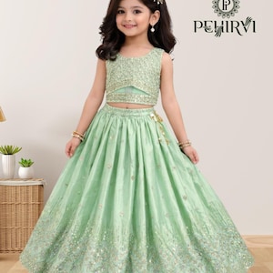 May include: A mint green two-piece outfit for a young girl. The sleeveless top and long skirt are embellished with sequins. The skirt has a flowing design. The outfit is from the brand PEHIRVI.