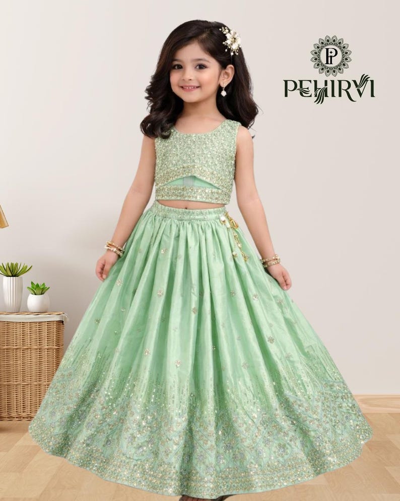 May include: A mint green two-piece outfit for a young girl. The sleeveless top and long skirt are embellished with sequins. The skirt has a flowing design. The outfit is from the brand PEHIRVI.