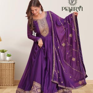 Peut inclure: Une longue robe violette avec des broderies dorées complexes sur le corsage, les manches et l'ourlet. La robe comprend un châle violet assorti avec des détails dorés. C'est une tenue formelle pour les occasions spéciales.