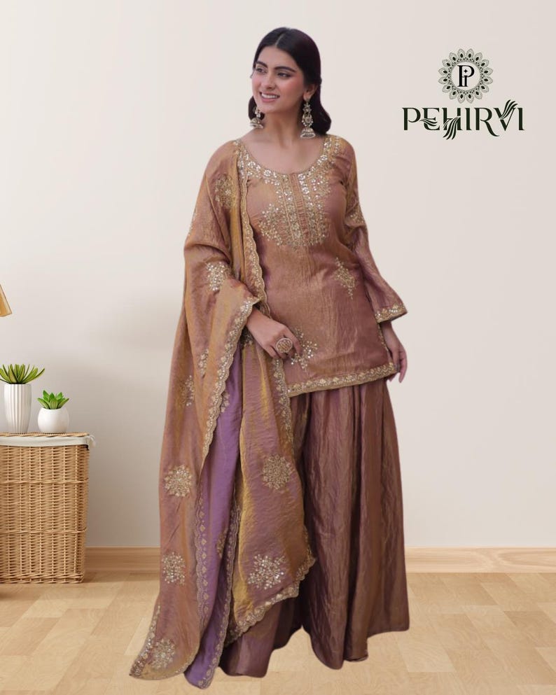 May include: A formal, two-piece outfit in shades of brown and purple. The top and dupatta feature intricate gold embroidery. The outfit is worn with matching wide-leg pants. The brand logo "PEHIRVI" is visible in the upper right corner.