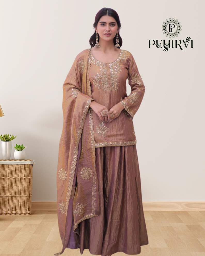 May include: A mauve-colored, embroidered salwar kameez set with a matching dupatta. The long-sleeved top and skirt are embellished with gold-colored embroidery. The dupatta is draped over the shoulder. The brand name "PEHIRVI" is visible in the upper right corner.