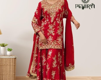 May include: A vibrant red sharara set featuring a long-sleeved tunic and wide-leg pants, both heavily embellished with intricate gold floral embroidery and sequins. A matching red dupatta with a gold border is draped over the shoulders.