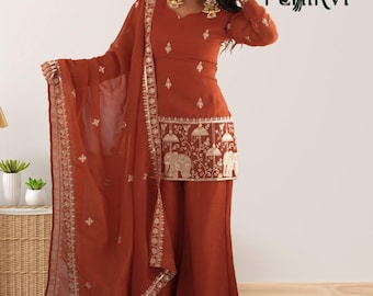 Puede incluir: Un conjunto de túnica de manga larga y pantalón ancho color óxido con un dupatta transparente a juego. La túnica presenta bordados dorados de elefantes y sombrillas en el dobladillo, con motivos florales. El logotipo PEHIRVI es visible.