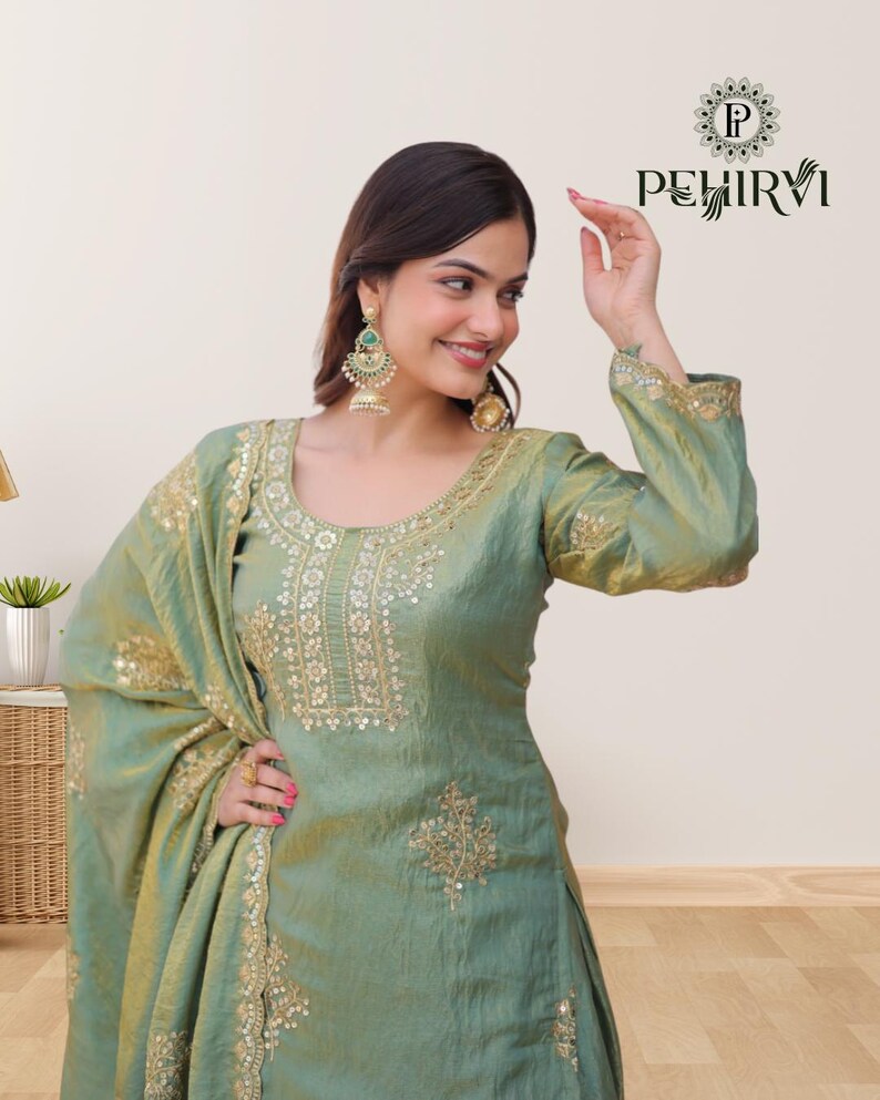 May include: A light green silk salwar kameez with gold embroidery and sequin embellishments. The outfit includes a matching dupatta and is adorned with intricate patterns. The image also shows a pair of gold earrings.