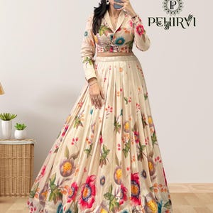 May include: A cream-colored two-piece outfit featuring a floral print. The long-sleeved top has a collared neckline and button closure. The matching skirt is pleated and flows to the floor. The floral pattern includes red, pink, blue, and yellow blooms.