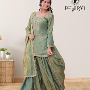 May include: Sage green Indian salwar kameez set with intricate gold embroidery. The set includes a long-sleeved tunic, wide-legged pants, and a matching scarf. The outfit features a textured fabric and decorative embellishments.