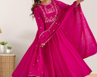 May include: A vibrant magenta-colored Anarkali suit with intricate embroidery around the neckline and sleeves. The long, flowing dress is paired with matching pants and a dupatta. The outfit features a flared silhouette and delicate detailing.