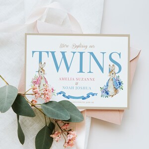 Puede incluir: Una tarjeta de invitaci&oacute;n de bautizo con una ilustraci&oacute;n de acuarela de dos conejos en azul y rosa. La tarjeta dice "We're Baptizing our Twins Amelia Suzanne & Noah Joshua. We'd love you to join us."