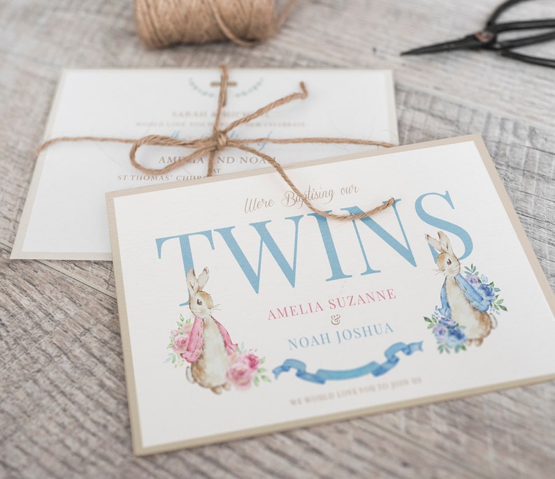 Puede incluir: Una tarjeta azul claro y blanca con el texto "Were Baptising our TWINS Amelia Suzanne & Noah Joshua" e ilustraciones de dos conejos, uno con una bufanda rosa y el otro con una bufanda azul.