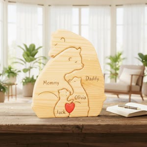 Puede incluir: Una escultura de madera de una familia de osos con las palabras "Mommy", "Daddy", "Olivia" y "Jack" grabadas. Un coraz&oacute;n rojo est&aacute; tallado entre los dos osos m&aacute;s peque&ntilde;os. La escultura est&aacute; hecha de madera clara y se exhibe sobre una mesa de madera.