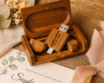 Könnte beinhalten: Ein hölzerner USB-Stick mit der Gravur "Sophie & Steve 10-25-2025" liegt in einer offenen Holzbox. Die Box enthält zwei Holzstücke und steht auf einem Tisch mit einer Hochzeitseinladung und floralen Akzenten. Die Farbpalette ist warm und natürlich.