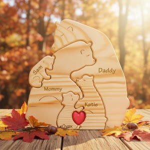 Puede incluir: Un rompecabezas de madera de una familia de osos con las palabras "Sam", "Mommy", "Katie", "Daddy" y "Ovnx" grabadas en las piezas. Un coraz&oacute;n rojo est&aacute; en el centro del rompecabezas. El rompecabezas est&aacute; sobre una superficie de madera con hojas de oto&ntilde;o.