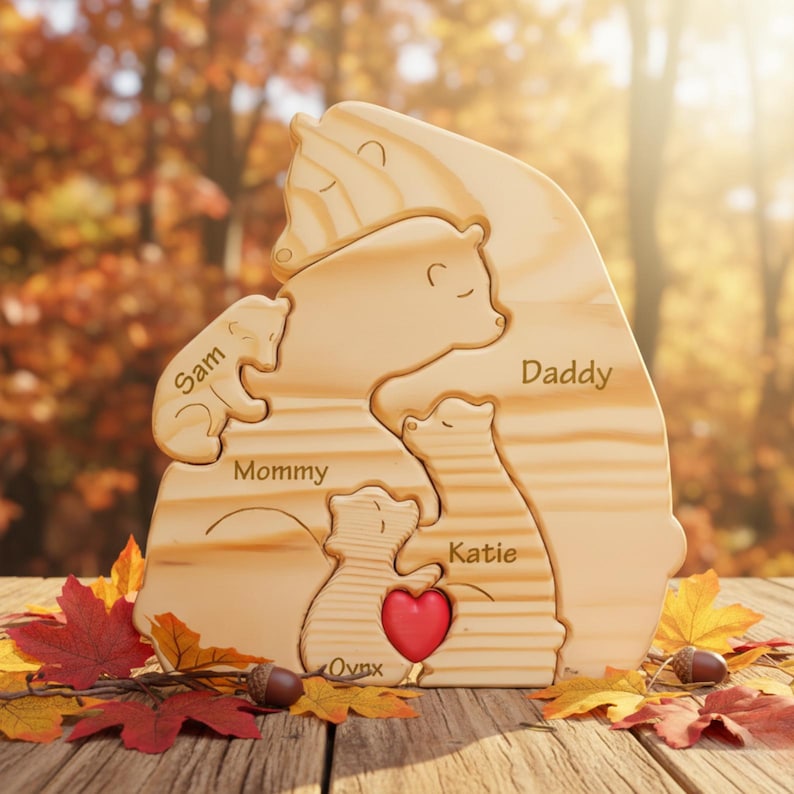 Puede incluir: Un rompecabezas de madera de una familia de osos con las palabras "Sam", "Mommy", "Katie", "Daddy" y "Ovnx" grabadas en las piezas. Un coraz&oacute;n rojo est&aacute; en el centro del rompecabezas. El rompecabezas est&aacute; sobre una superficie de madera con hojas de oto&ntilde;o.
