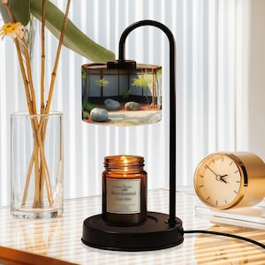 以下が含まれることがあります： 日本の庭園の風景が描かれた円筒形のシェードが付いた黒いキャンドルウォーマー。茶色の瓶に入った火の灯ったキャンドルがベースに置かれています。背景には金色の時計が見えます。