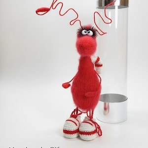 May include: A handmade red plush creature with googly eyes, wearing white and red sneakers. The creature has a whimsical design with a curly red antenna and white and red striped arms. The text "Handmade Gift li-lu.co.uk" is at the bottom.