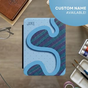 May include: A light blue tablet case with the name "JAKE" printed on it. The case has a blue wavy design over a striped pattern in blue and purple. The text "CUSTOM NAME AVAILABLE!" is in a blue circle.