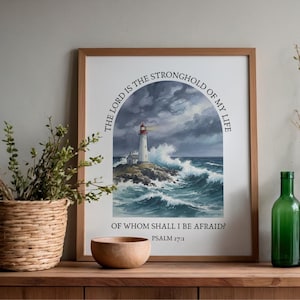 May include: Framed art print featuring a lighthouse on a rocky island, with crashing waves under a stormy sky. The text reads "The Lord is the stronghold of my life. Of whom shall I be afraid? Psalm 27:1". The frame is brown.