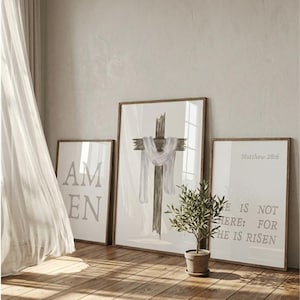 Puede incluir: Tres impresiones artísticas enmarcadas con temática religiosa. La impresión central presenta una cruz de madera rústica con un paño blanco. La impresión izquierda dice "AM EN" y la derecha dice "HE IS NOT HERE: FOR HE IS RISEN".