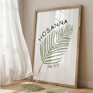May include: A framed print with the word "HOSANNA" in black script above a green watercolor palm leaf. The text "John 12:13" is below the leaf. The frame is made of light brown wood.