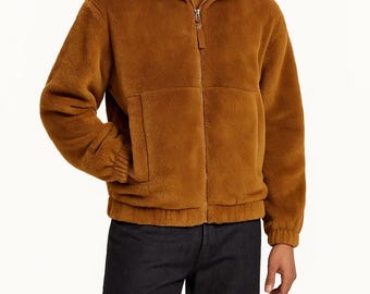Può includere: Giacca in pile marrone con collo alto e cerniera a tutta lunghezza. La giacca ha due tasche anteriori e polsini e orlo a coste. La modella indossa una camicia marrone e jeans neri.