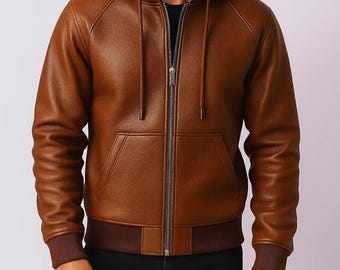 May include: A brown leather hooded jacket with a full-length zipper, front pockets, and ribbed cuffs and hem. The jacket has a hood with drawstrings and a dark brown lining. The model is wearing a black shirt underneath.