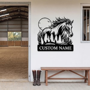 May include: Black metal horse silhouette with a flowing mane, set against a forest and a full moon. The design includes the text "CUSTOM NAME" on a rectangular plaque. The artwork is mounted on a white wall.