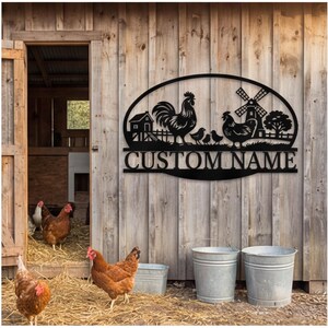 May include: A black metal wall sign featuring a farm scene with a rooster, a hen, two chicks, a barn, and a windmill. The design is enclosed in an oval frame with the text CUSTOM NAME centered below the illustration in a bold serif font.