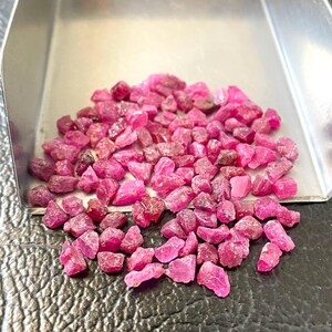 Könnte beinhalten: Eine Sammlung roher, ungeschliffener Rubin-Edelsteine. Die rohen Rubine haben eine tiefrosa-rote Farbe und befinden sich in einer kleinen, silbernen Metallschale. Die Edelsteine sind verstreut und zeigen ihre unregelmäßigen Formen und natürlichen Texturen.