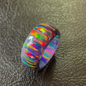 Può includere: Un vivace anello in opale multicolore. L'anello mostra uno spettro di colori, tra cui rosso, arancione, giallo, verde e blu, creando un effetto arcobaleno. La superficie lucida riflette la luce, evidenziando gli intricati motivi all'interno della gemma.