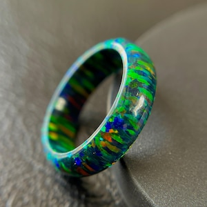 Peut inclure: Une bague vibrante avec un design irisé coloré. La bague présente un mélange de teintes vertes, bleues et oranges, créant une apparence unique et accrocheuse. La surface de la bague a une finition brillante.