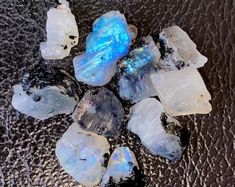 May include: A collection of raw moonstone crystals. The stones vary in size and shape, displaying a range of colors from translucent white to deep blue and black. Some stones have a shimmering, iridescent quality.
