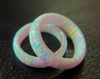 May include: Two opal rings with a rainbow iridescence. The rings are a light pink color and have a smooth, polished surface. The rings are set against a dark background.