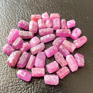Könnte beinhalten: Eine Sammlung roher, ungeschliffener Rubin-Edelsteine. Die Steine variieren in Größe und Form und weisen eine Reihe von rosa und roten Farbtönen auf. Die raue Textur der Edelsteine ist sichtbar, wobei einige eine leicht durchscheinende Qualität aufweisen.