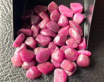Peut inclure: Un ensemble de pierres précieuses rubis polies et roulées de tailles et de formes variées. Les pierres précieuses sont d'une couleur rouge-rosé profond et vibrante, avec une surface lisse et légèrement réfléchissante. Elles sont contenues dans un petit plateau noir.