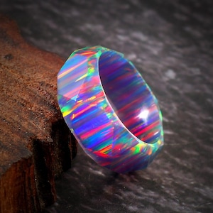 May include: A faceted opal ring displaying a spectrum of colors, including blue, green, and red. The ring is set against a dark background, highlighting its iridescent qualities. The gemstone's unique pattern is visible.