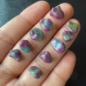 Peut inclure: Une collection de petites pierres précieuses de rubis brutes. Les rubis présentent un mélange de couleurs rouge foncé et sarcelle, certains montrant des nuances de vert. Les pierres ont des formes irrégulières et un aspect naturel, non poli.