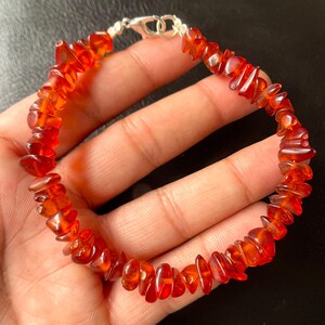 May include: A bracelet made of polished, irregular amber-coloured stones. The stones are strung together and secured with a silver-coloured clasp. The translucent stones create a simple and elegant design.