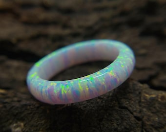 May include: A white opal ring with iridescent flashes of green, blue, and yellow. The ring is smooth and polished, showcasing the natural play-of-color of the opal. The ring is a band style, perfect for everyday wear.